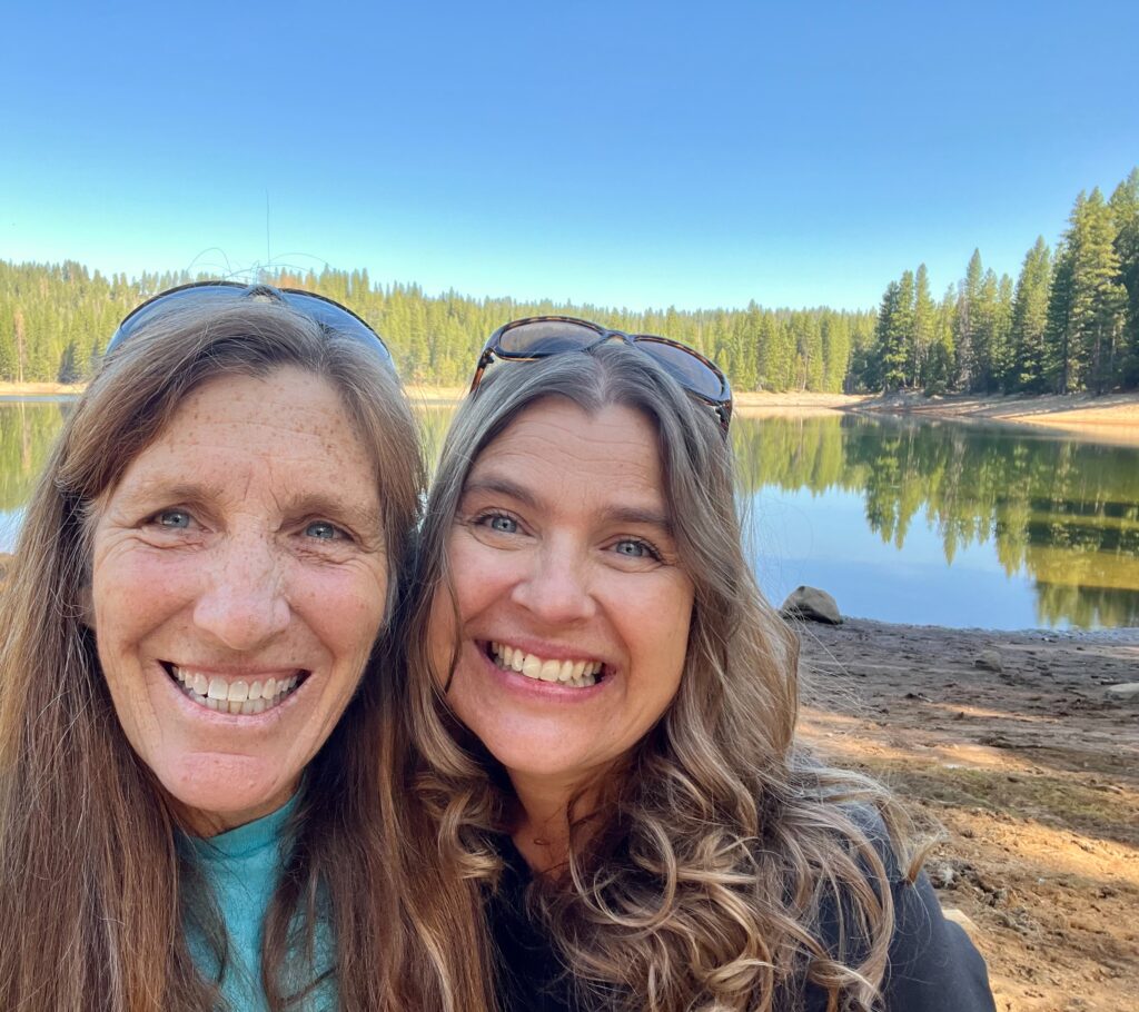 Christina and Heidi smiling together by a mountain lake
